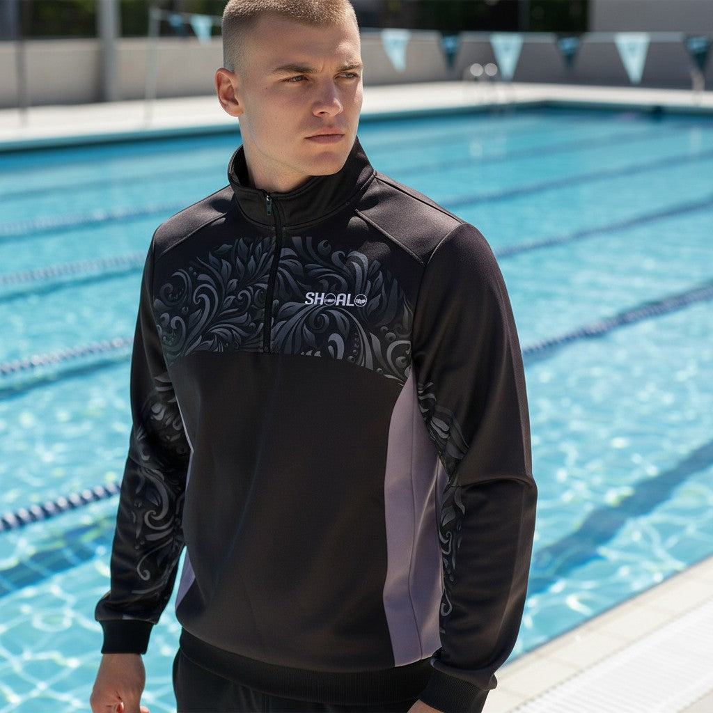 Waterpoloshop unisex black quarter zip top with grey side panels and ornate pattern, worn by a man at a pool.